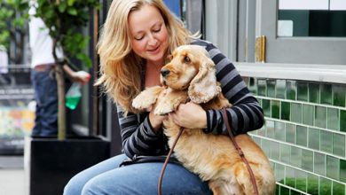 A woman cuddling a dog sat on a bench smiling.