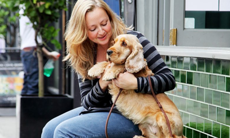 A woman cuddling a dog sat on a bench smiling.