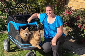 Westies on Wheels; a westie in a dog pram with it's owner crouched next to him.